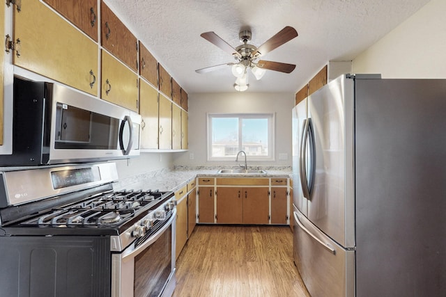 kitchen with a ceiling fan, a sink, stainless steel appliances, light wood-style floors, and a textured ceiling