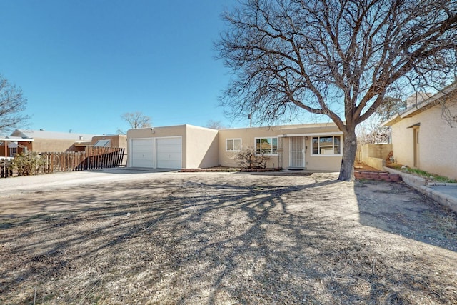 adobe home featuring stucco siding, a garage, and fence