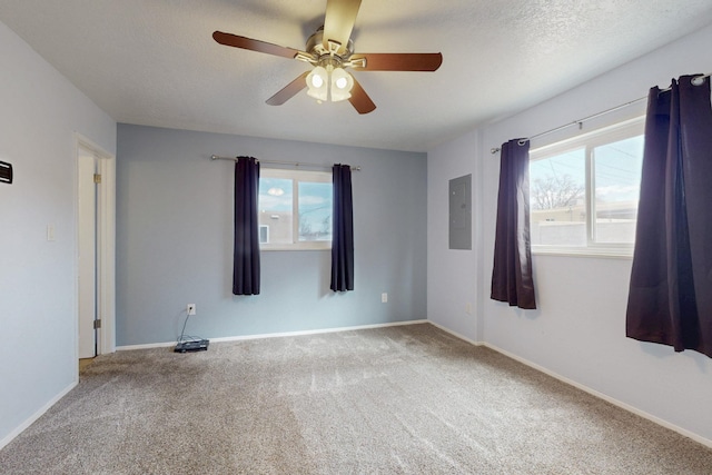 empty room featuring a wealth of natural light, carpet floors, electric panel, and a ceiling fan