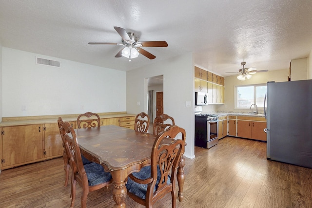 dining space with a textured ceiling, light wood-style floors, visible vents, and ceiling fan