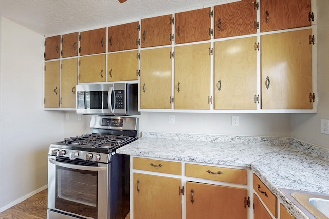 kitchen with baseboards, light countertops, stainless steel appliances, wood finished floors, and a textured ceiling