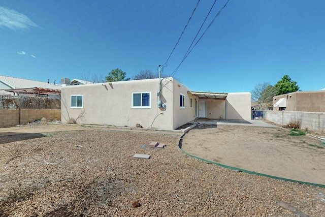 rear view of property featuring fence and stucco siding