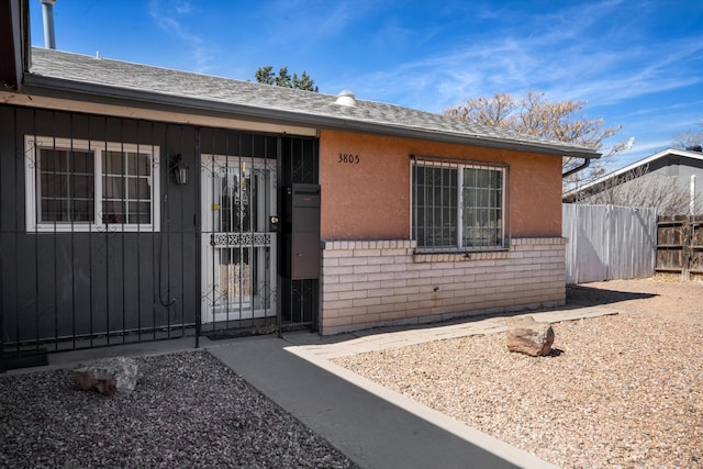 doorway to property with brick siding, a shingled roof, and fence