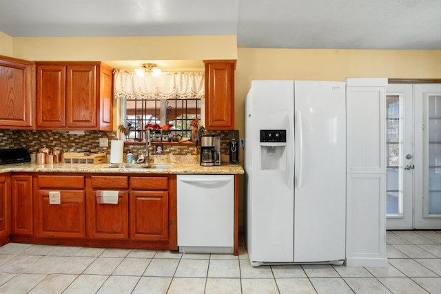 kitchen featuring a sink, backsplash, white appliances, light tile patterned flooring, and brown cabinetry