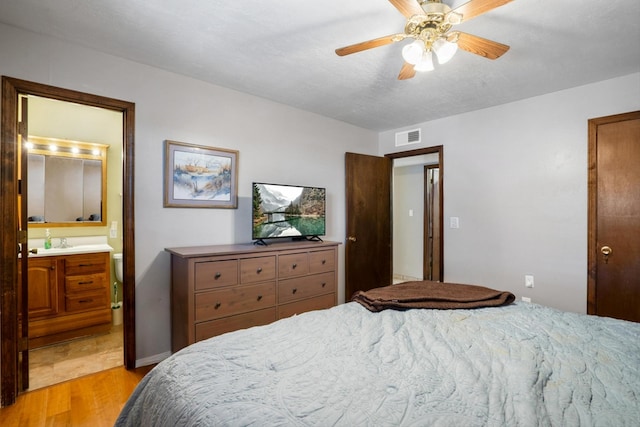 bedroom featuring visible vents, a sink, ensuite bath, light wood-style floors, and ceiling fan