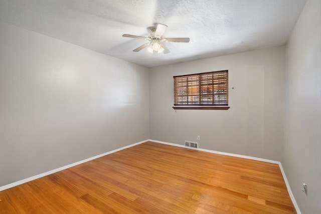 spare room featuring light wood finished floors, visible vents, baseboards, a textured ceiling, and a ceiling fan