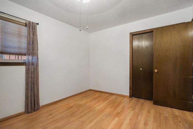 unfurnished bedroom featuring baseboards, light wood-type flooring, and a closet