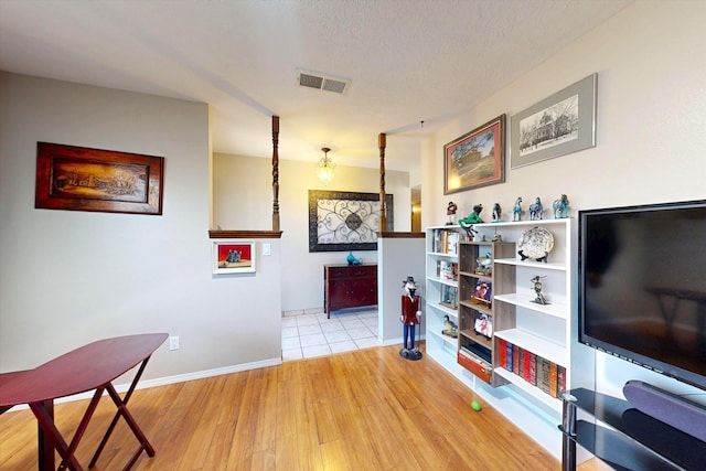 corridor featuring visible vents, baseboards, light wood-style floors, and a textured ceiling