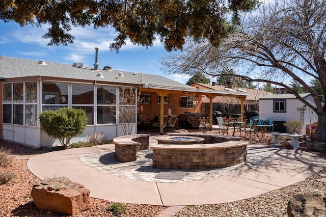 back of property featuring a patio area, a fire pit, an outbuilding, and a sunroom