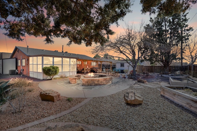 back of property at dusk featuring central air condition unit, a patio, a fire pit, and fence