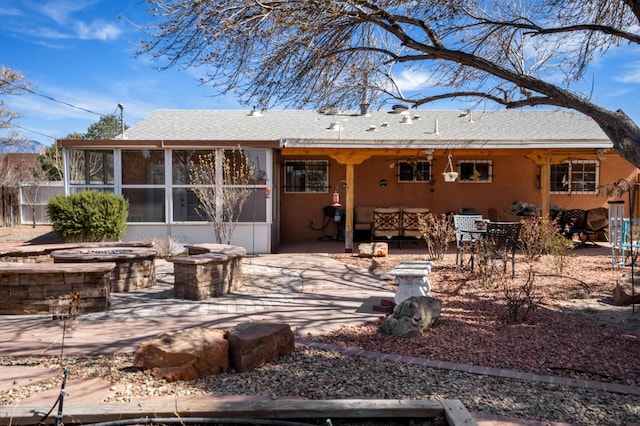 rear view of property with stucco siding, a patio, a sunroom, a fire pit, and a shingled roof