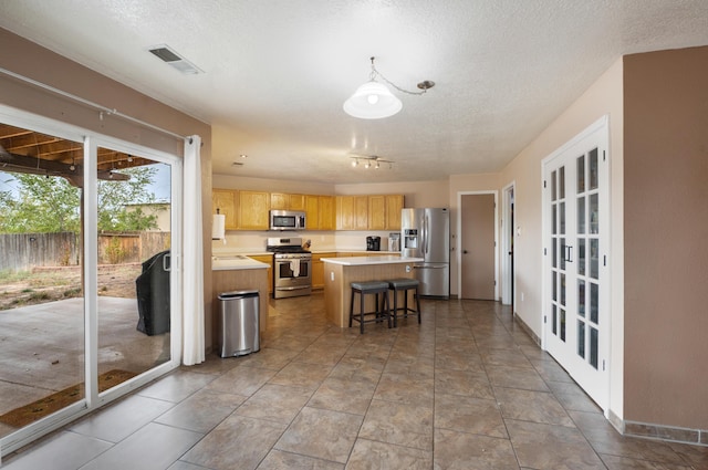 101 Colinas Ave NE, Albuquerque, NM 87113 - kitchen with visible vents, a textured ceiling, a kitchen island, appliances with stainless steel finishes, and light countertops