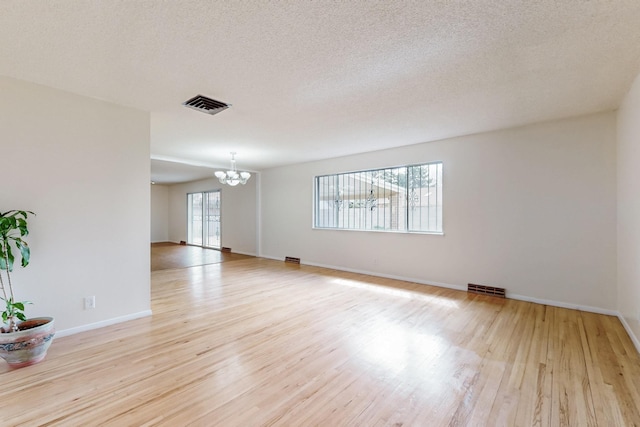 unfurnished room featuring a chandelier, visible vents, a textured ceiling, and light wood-style floors