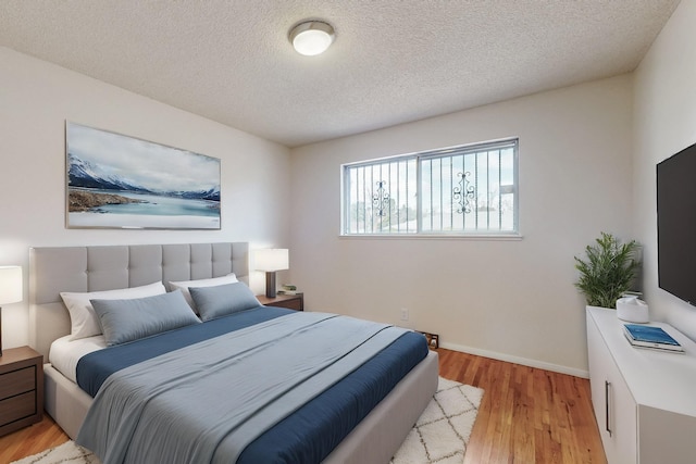 bedroom featuring baseboards, a textured ceiling, and light wood-style flooring