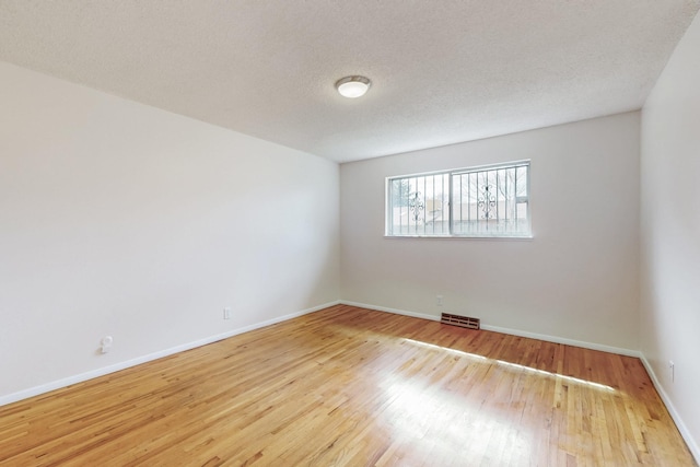 empty room with a textured ceiling, wood finished floors, visible vents, and baseboards