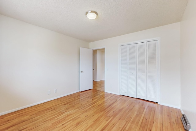 unfurnished bedroom featuring a closet, baseboards, a textured ceiling, and light wood finished floors