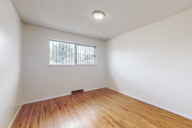 unfurnished room with a textured ceiling, light wood-style floors, visible vents, and baseboards