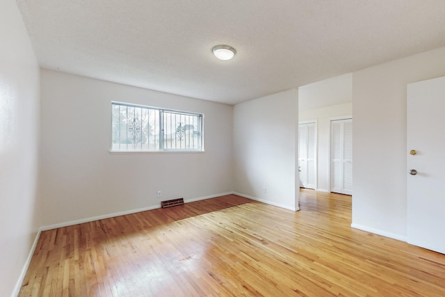 empty room with light wood-style floors, visible vents, and baseboards