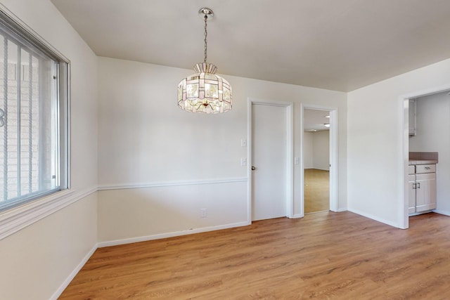 unfurnished dining area with an inviting chandelier, light wood-style floors, and baseboards