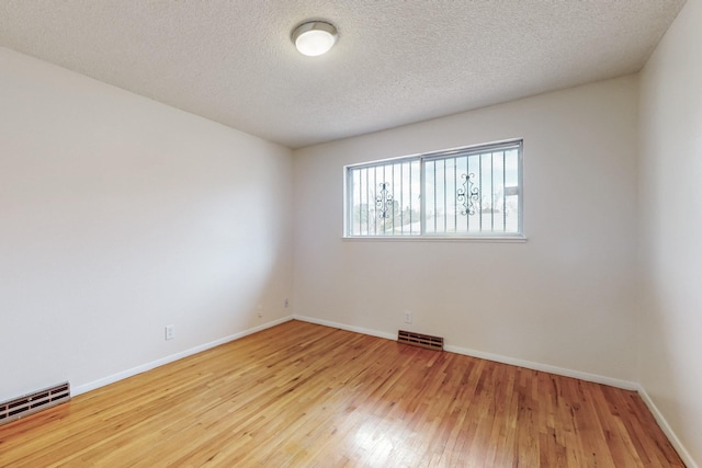 spare room featuring hardwood / wood-style floors, baseboards, visible vents, and a baseboard radiator