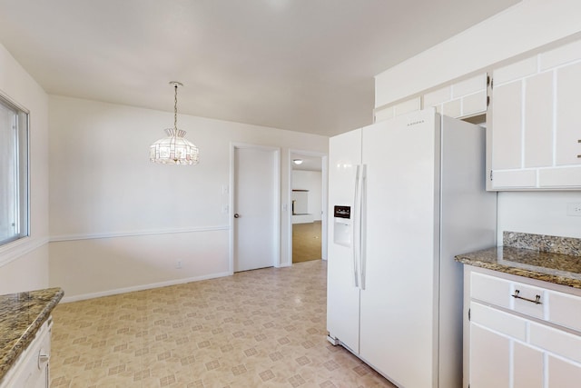 kitchen with dark stone counters, white fridge with ice dispenser, white cabinetry, decorative light fixtures, and a notable chandelier