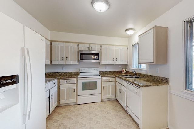 kitchen featuring white appliances, dark stone countertops, and a sink