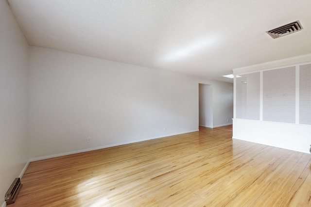 empty room with baseboards, light wood-style flooring, visible vents, and baseboard heating