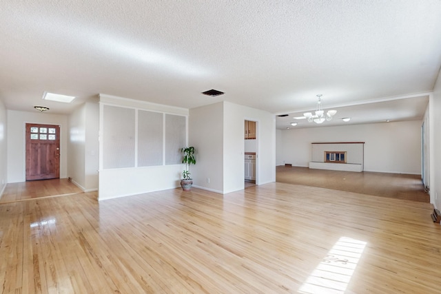 unfurnished living room featuring baseboards, wood finished floors, a textured ceiling, and a chandelier