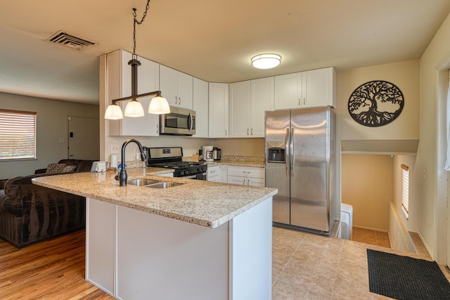 kitchen with light stone countertops, a peninsula, a sink, appliances with stainless steel finishes, and white cabinetry