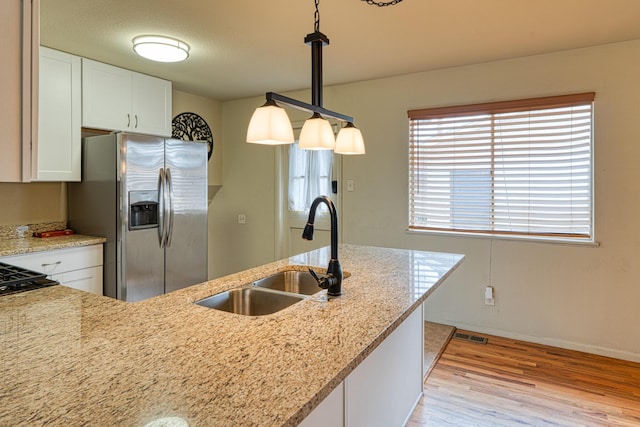 kitchen featuring decorative light fixtures, light wood-type flooring, white cabinets, stainless steel fridge, and a sink