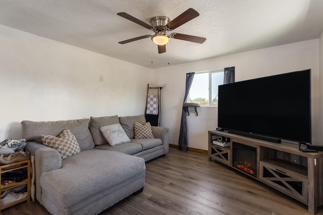 living room featuring a textured ceiling, wood finished floors, baseboards, and a ceiling fan