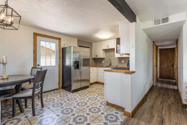 kitchen with a textured ceiling, stainless steel fridge with ice dispenser, white cabinetry, and visible vents