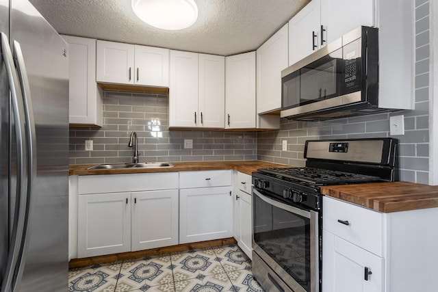 kitchen with tasteful backsplash, a sink, wooden counters, appliances with stainless steel finishes, and a textured ceiling