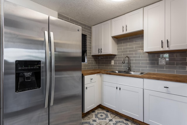 kitchen featuring white cabinets, stainless steel refrigerator with ice dispenser, a sink, a textured ceiling, and wood counters