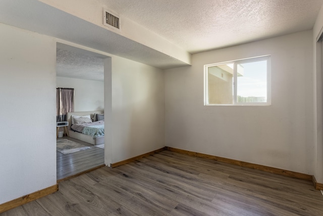 unfurnished room with a textured ceiling, wood finished floors, baseboards, and visible vents