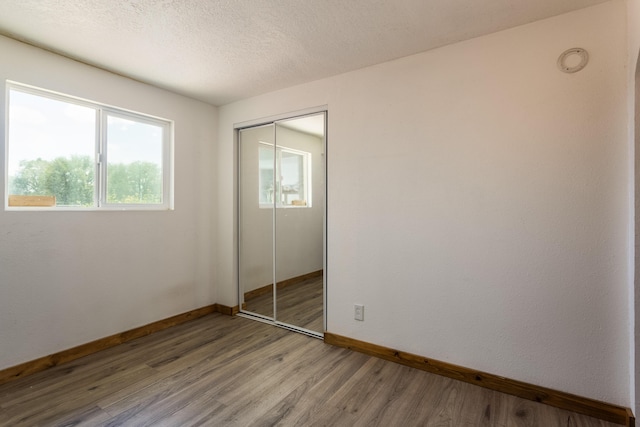 unfurnished bedroom with a closet, baseboards, light wood finished floors, and a textured ceiling