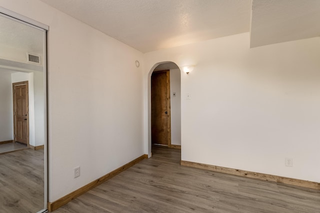 empty room with visible vents, baseboards, arched walkways, and wood finished floors