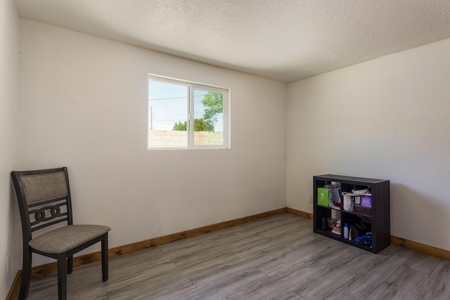 unfurnished room featuring baseboards, light wood finished floors, and a textured ceiling