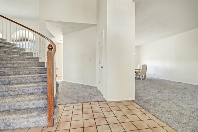 stairway featuring tile patterned floors, baseboards, carpet floors, and a towering ceiling