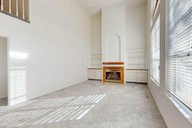 unfurnished living room with light carpet, a fireplace with flush hearth, visible vents, and a towering ceiling