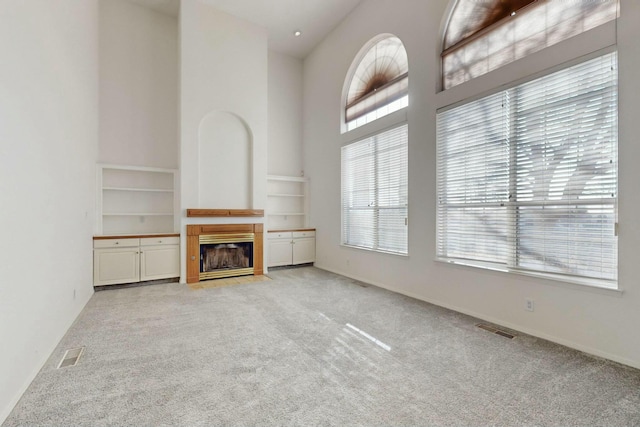 unfurnished living room with a high ceiling, a fireplace with flush hearth, carpet, and visible vents