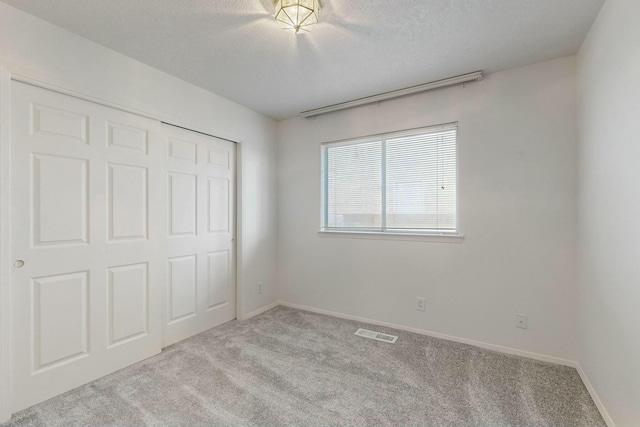unfurnished bedroom featuring carpet flooring, visible vents, a closet, and a textured ceiling