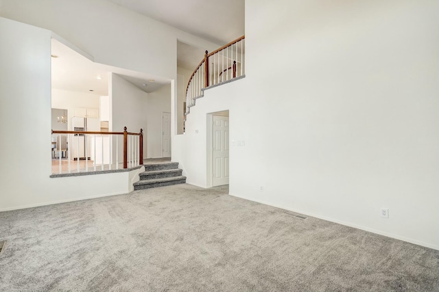 unfurnished living room with carpet flooring, baseboards, a towering ceiling, and stairs