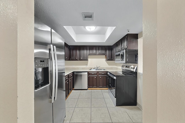 kitchen with visible vents, dark brown cabinetry, a raised ceiling, light tile patterned floors, and stainless steel appliances