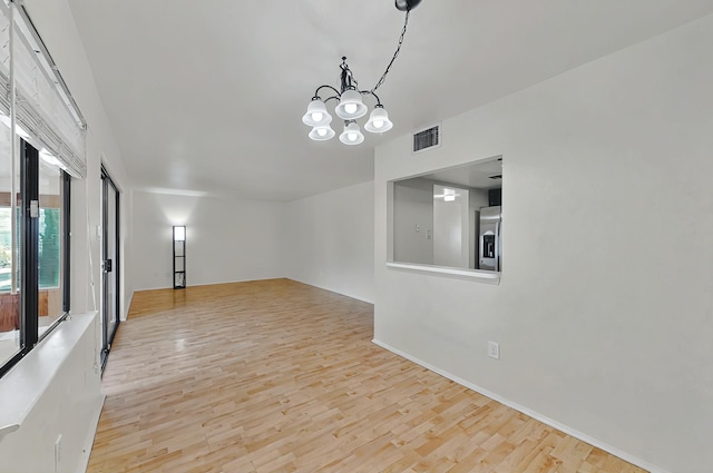 spare room featuring an inviting chandelier, baseboards, wood finished floors, and visible vents