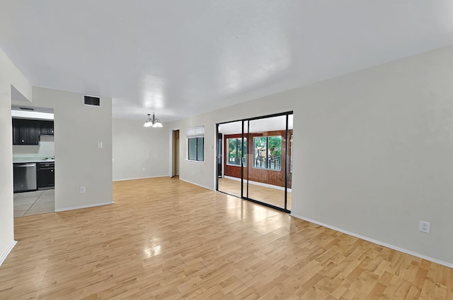unfurnished living room featuring baseboards, a notable chandelier, visible vents, and light wood-type flooring