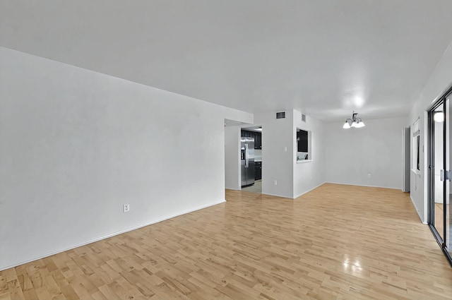 unfurnished living room featuring visible vents, an inviting chandelier, and light wood finished floors