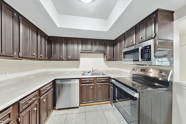 kitchen with a tray ceiling, dark brown cabinets, a sink, light tile patterned floors, and stainless steel appliances
