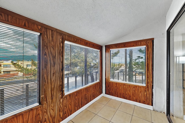 unfurnished sunroom featuring tile patterned floors, a textured ceiling, lofted ceiling, and wood walls