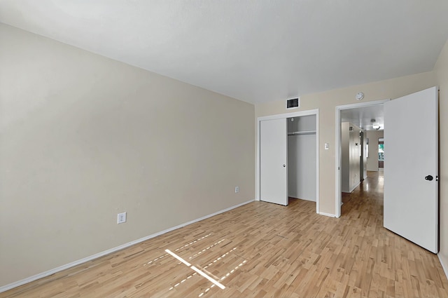 unfurnished bedroom featuring light wood-style floors, baseboards, visible vents, and a closet